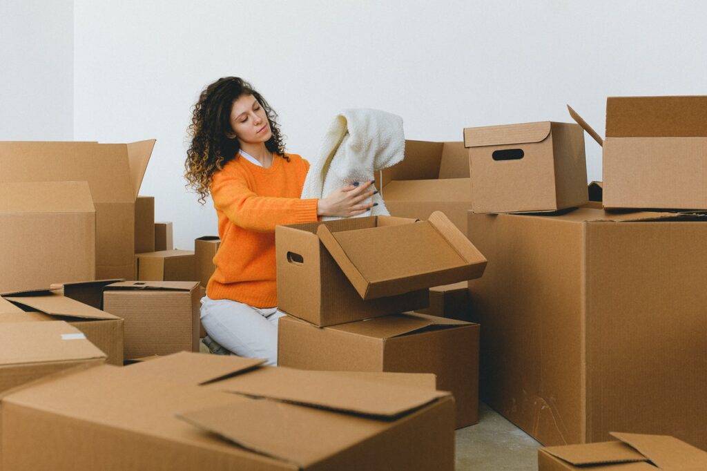 Thoughtful young lady packing clothes into boxes during relocating